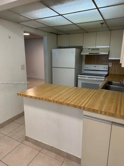 17890 W Dixie Hwy Unit 219, Miami, FL 33160 - kitchen with white appliances, under cabinet range hood, light tile patterned floors, a peninsula, and butcher block counters