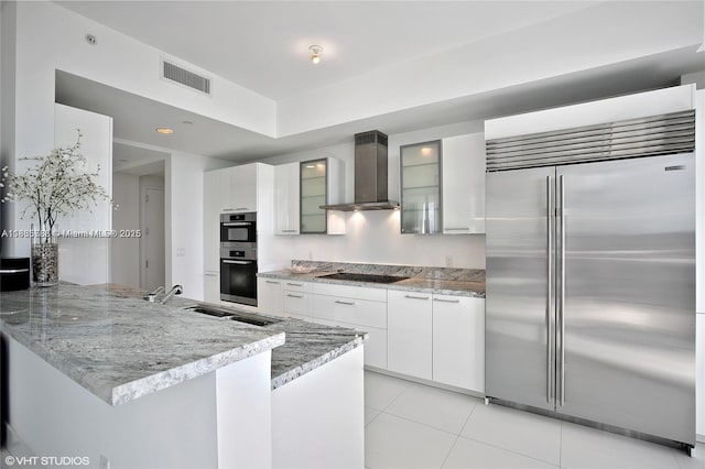 4100 Island Blvd Unit 701, Aventura, FL 33160 - kitchen featuring appliances with stainless steel finishes, wall chimney exhaust hood, a peninsula, glass insert cabinets, and light tile patterned floors