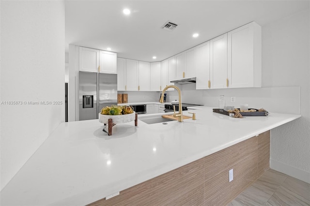500 NW 7th Ct, Hallandale Beach, FL 33009 - kitchen featuring stainless steel fridge with ice dispenser, a peninsula, under cabinet range hood, white cabinets, and recessed lighting