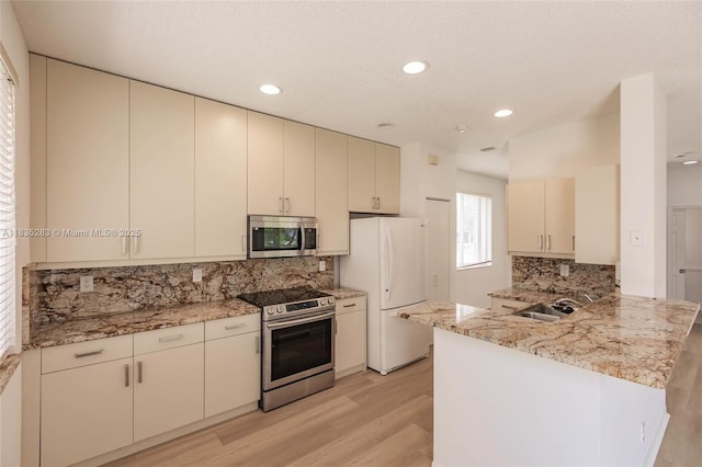 1326 Majesty Ter, Weston, FL 33327 - kitchen with appliances with stainless steel finishes, a peninsula, cream cabinetry, light wood finished floors, and backsplash