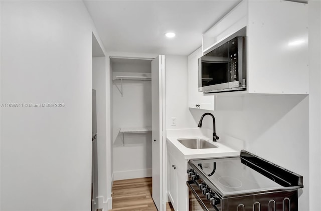 1260 SW 4th St, Miami, FL 33135 - kitchen with stainless steel microwave, black range with electric stovetop, white cabinetry, light wood-style flooring, and light countertops