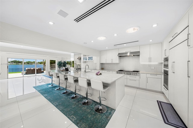 1930 NE 193rd St, Miami, FL 33179 - kitchen with stainless steel gas cooktop, light tile patterned flooring, white cabinetry, under cabinet range hood, and tasteful backsplash