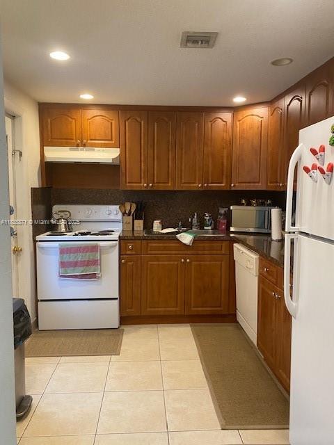 14150 SW 84th St Unit 201-I, Miami, FL 33183 - kitchen featuring white appliances, under cabinet range hood, light tile patterned floors, brown cabinets, and dark countertops