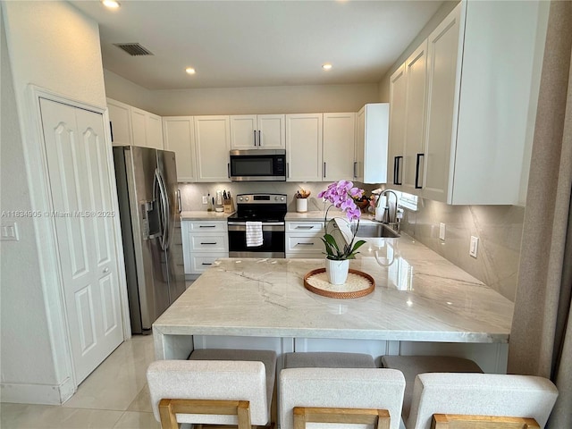 14902 SW 23rd Way, Miami, FL 33185 - kitchen with stainless steel appliances, a peninsula, white cabinetry, light stone counters, and a kitchen bar