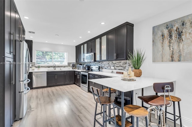 11433 NE 6th Ave, Biscayne Park, FL 33161 - kitchen with stainless steel appliances, light wood-type flooring, decorative backsplash, a kitchen bar, and a peninsula