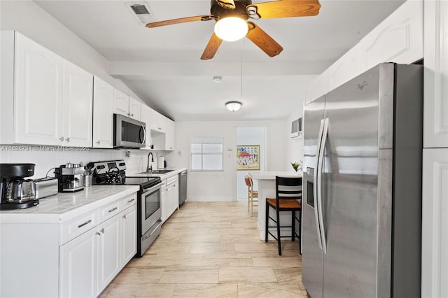 2946 SW 26th St, Miami, FL 33133 - kitchen with appliances with stainless steel finishes, light countertops, white cabinetry, ceiling fan, and a breakfast bar