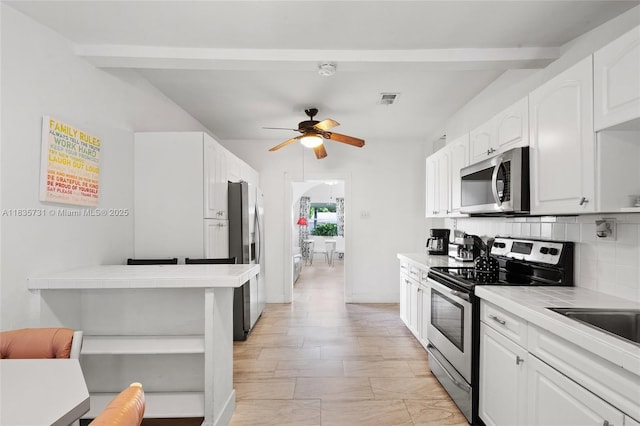 2946 SW 26th St, Miami, FL 33133 - kitchen featuring stainless steel appliances, white cabinetry, tasteful backsplash, a ceiling fan, and tile counters