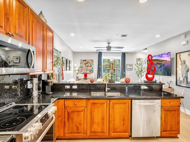 2249 NE 9th Ave, Wilton Manors, FL 33305 - kitchen featuring appliances with stainless steel finishes, dark stone counters, ceiling fan, brown cabinetry, and a peninsula
