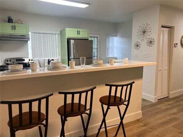 8921 NW 17th Ave, Miami, FL 33147 - kitchen featuring appliances with stainless steel finishes, green cabinetry, under cabinet range hood, and a breakfast bar area