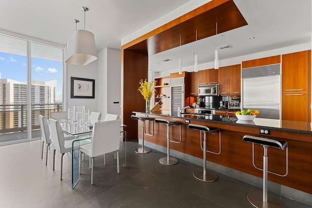 901 Brickell Key Blvd Unit 3607, Miami, FL 33131 - kitchen featuring stainless steel appliances, a kitchen breakfast bar, brown cabinetry, a wall of windows, and tasteful backsplash