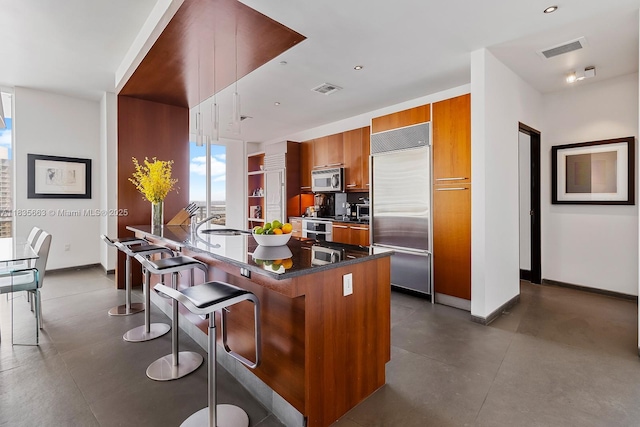 901 Brickell Key Blvd Unit 3607, Miami, FL 33131 - kitchen with stainless steel appliances, brown cabinetry, a kitchen bar, dark countertops, and modern cabinets