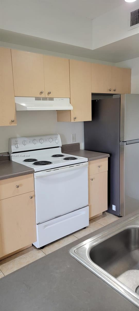 2452 Centergate Dr Unit 103, Miramar, FL 33025 - kitchen featuring white range with electric stovetop, freestanding refrigerator, under cabinet range hood, cream cabinetry, and dark countertops