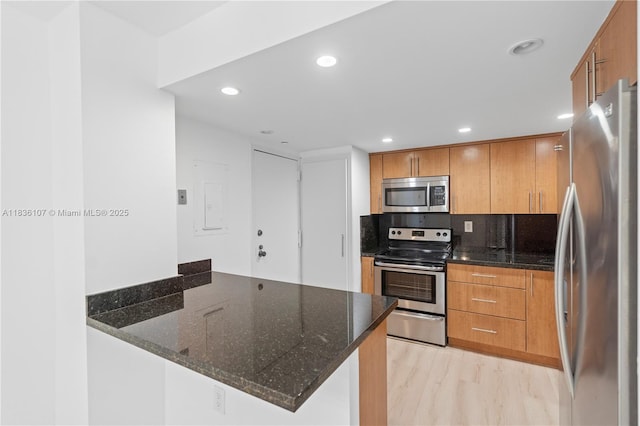 2333 Brickell Ave Unit 1908, Miami, FL 33129 - kitchen featuring stainless steel appliances, a peninsula, brown cabinetry, recessed lighting, and dark stone counters