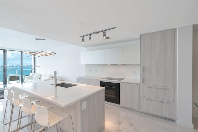 3131 NE 7th Ave Unit 1202, Miami, FL 33137 - kitchen featuring black appliances, modern cabinets, a center island with sink, light marble finish flooring, and light countertops