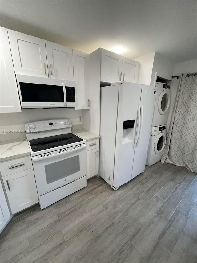 2173 NW 78th Ave Unit 103, Pembroke Pines, FL 33024 - kitchen featuring white appliances, stacked washer / drying machine, white cabinetry, light wood finished floors, and light stone countertops