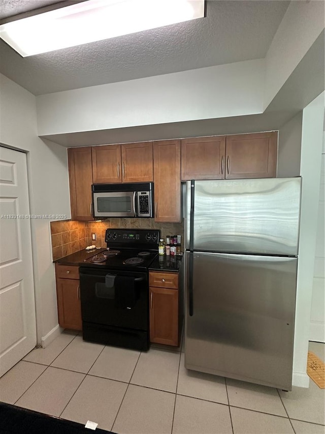 2000 N Bayshore Dr Unit 1505, Miami, FL 33137 - kitchen featuring stainless steel appliances, dark countertops, light tile patterned floors, decorative backsplash, and brown cabinetry