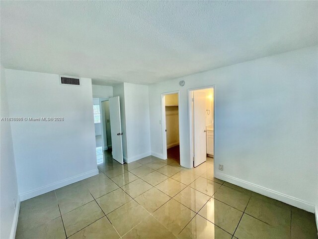 241 SE 9th Ave Unit 207, Pompano Beach, FL 33060 - unfurnished bedroom with a textured ceiling, light tile patterned floors, a walk in closet, a closet, and connected bathroom