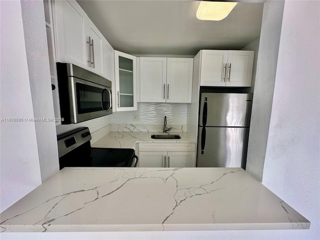 241 SE 9th Ave Unit 207, Pompano Beach, FL 33060 - kitchen with appliances with stainless steel finishes, glass insert cabinets, light stone counters, white cabinetry, and a textured wall