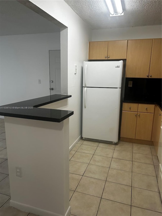 7110 NW 179th St Unit 110, Hialeah, FL 33015 - kitchen featuring freestanding refrigerator, dark countertops, light tile patterned floors, a peninsula, and a textured ceiling