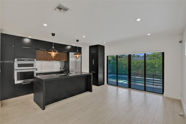 120 NW 41st St, Miami, FL 33127 - kitchen featuring modern cabinets, stainless steel double oven, dark countertops, a kitchen island with sink, and light wood finished floors