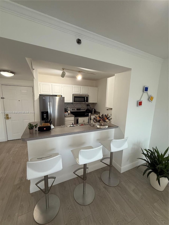 2665 SW 37th Ave Unit 1213, Miami, FL 33133 - kitchen featuring appliances with stainless steel finishes, a kitchen bar, ornamental molding, a peninsula, and wood finished floors