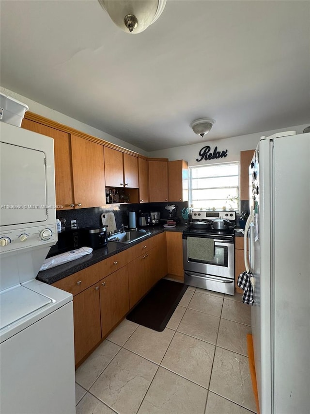 2651 NW 13th St Unit 45, Miami, FL 33125 - kitchen featuring freestanding refrigerator, stainless steel electric range, stacked washer / drying machine, brown cabinets, and light tile patterned floors