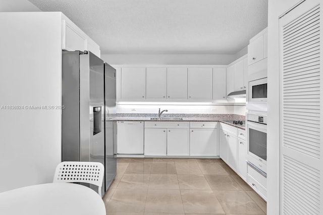 8855 E Collins Ave Unit 2F, Surfside, FL 33154 - kitchen featuring white appliances, under cabinet range hood, white cabinetry, a textured ceiling, and light stone counters