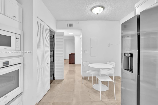 8855 E Collins Ave Unit 2F, Surfside, FL 33154 - kitchen featuring white appliances, a textured ceiling, light tile patterned floors, white cabinetry, and light countertops