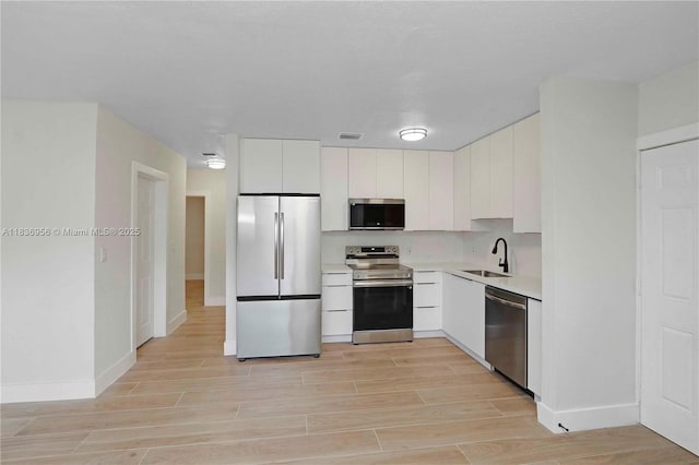 990 NE 159th St, North Miami Beach, FL 33162 - kitchen featuring appliances with stainless steel finishes, light wood-style flooring, light countertops, white cabinets, and modern cabinets