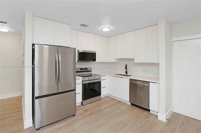 990 NE 159th St, North Miami Beach, FL 33162 - kitchen featuring appliances with stainless steel finishes, light wood-style flooring, light countertops, and white cabinetry
