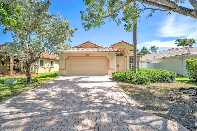 mediterranean / spanish-style home with stucco siding, an attached garage, a tiled roof, and decorative driveway
