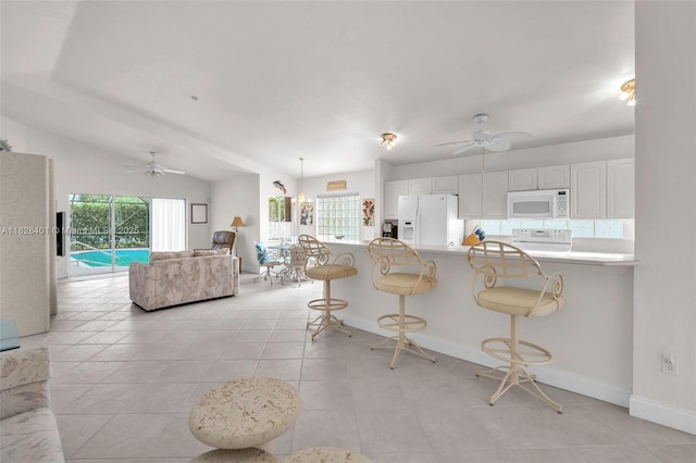 kitchen with white appliances, ceiling fan, and a breakfast bar area