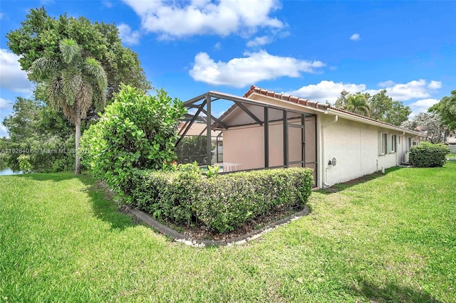 rear view of property featuring stucco siding, a yard, a tiled roof, and a lanai