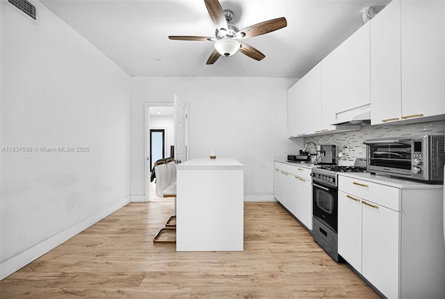 11055 NW 59th Ct, Hialeah, FL 33012 - kitchen featuring gas stove, ceiling fan, backsplash, under cabinet range hood, and white cabinetry