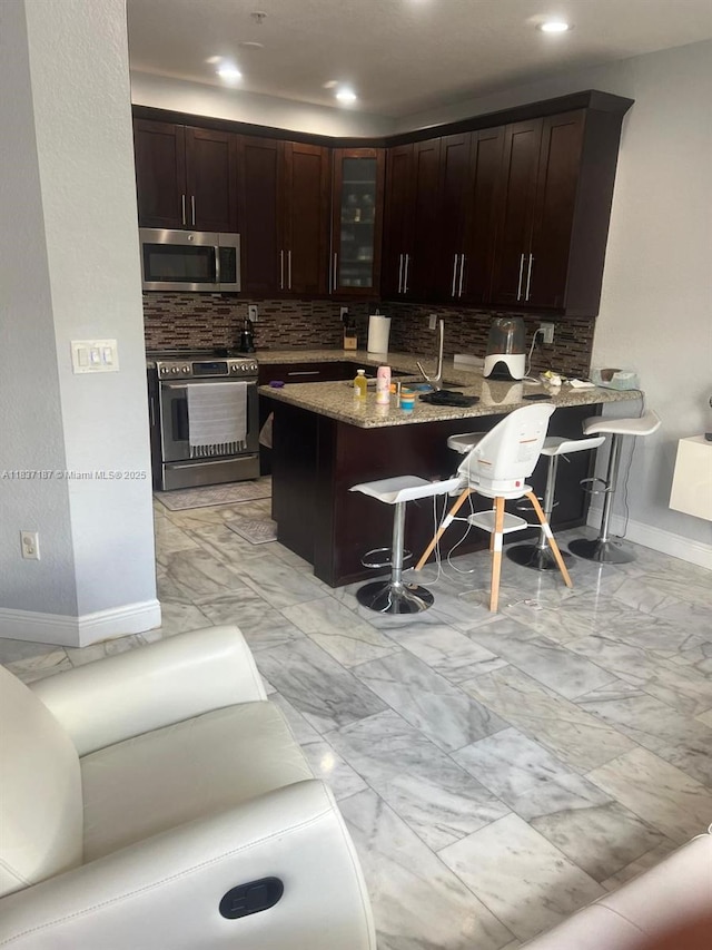 4301 SW 160th Ave Unit 215, Miramar, FL 33027 - kitchen featuring stainless steel appliances, a breakfast bar area, decorative backsplash, glass insert cabinets, and recessed lighting