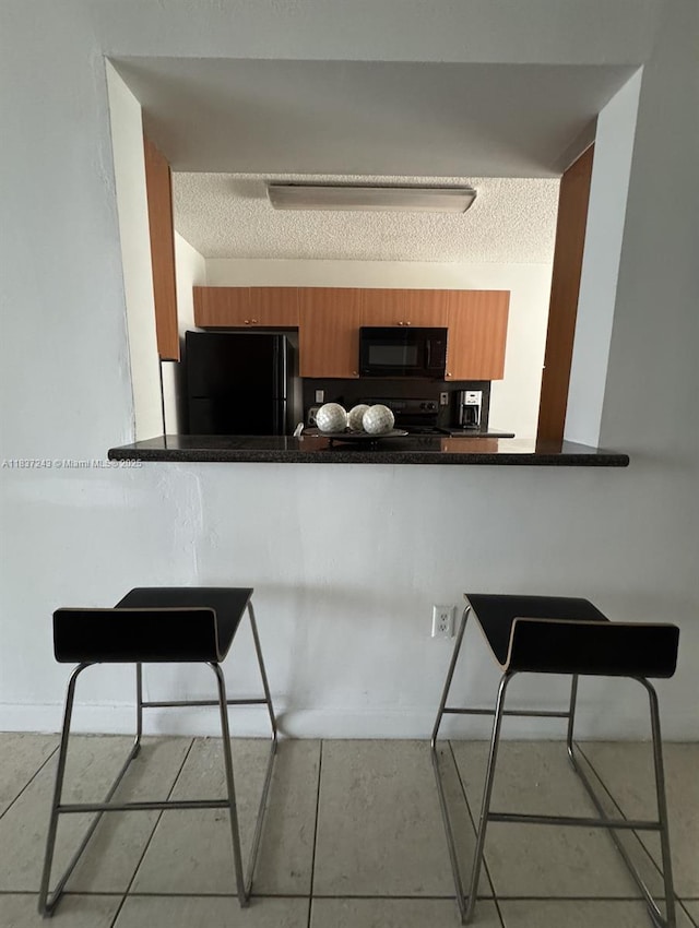 9755 NW 48th Ter Unit 321, Doral, FL 33178 - kitchen featuring black appliances, brown cabinets, a kitchen bar, dark countertops, and a textured ceiling