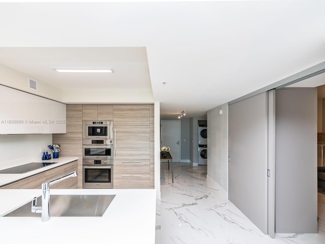300 Sunny Isles Blvd Unit 5-1605, Sunny Isles Beach, FL 33160 - kitchen with estacked washer and dryer, modern cabinets, black electric stovetop, stainless steel double oven, and light countertops