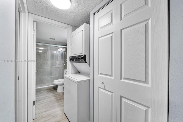 8821 NW 38th Dr Unit 103A, Coral Springs, FL 33065 - washroom featuring stacked washer and clothes dryer, light wood-type flooring, and a textured ceiling