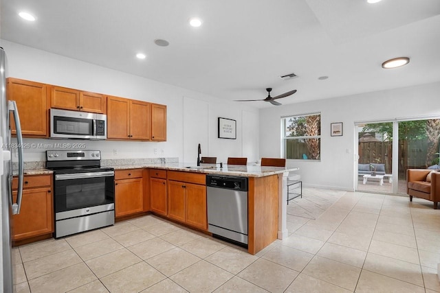 4326 Braxton Ave, West Palm Beach, FL 33417 - kitchen with stainless steel appliances, a peninsula, brown cabinetry, light tile patterned flooring, and recessed lighting
