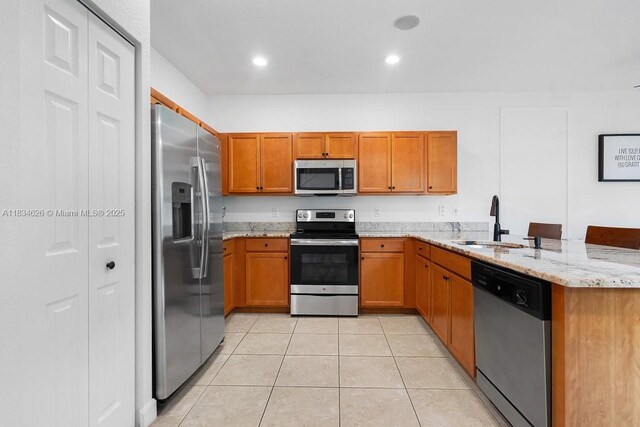 4326 Braxton Ave, West Palm Beach, FL 33417 - kitchen with appliances with stainless steel finishes, brown cabinets, a peninsula, light tile patterned floors, and light stone counters
