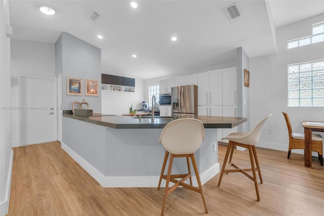 16410 Sapphire Bnd, Weston, FL 33331 - kitchen featuring stainless steel refrigerator with ice dispenser, a peninsula, dark countertops, a breakfast bar area, and light wood finished floors