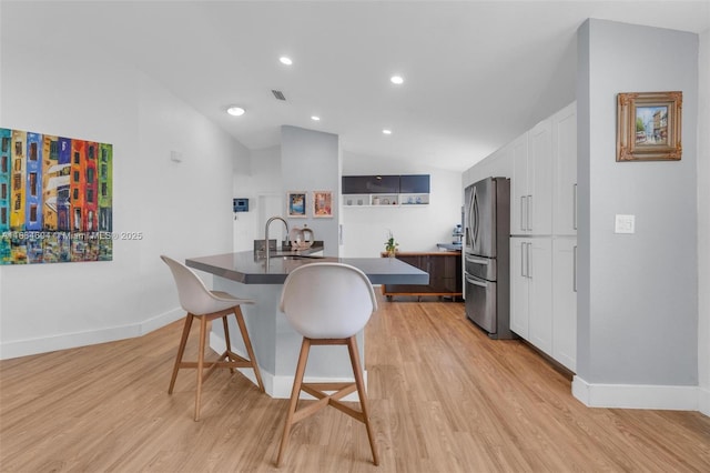 16410 Sapphire Bnd, Weston, FL 33331 - kitchen featuring stainless steel fridge, a kitchen bar, vaulted ceiling, light wood-type flooring, and white cabinetry