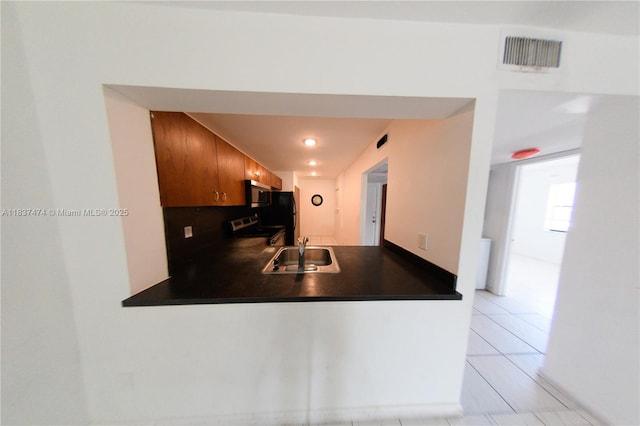 20825 NE 8th Ct Unit 203-19, Miami, FL 33179 - kitchen with dark countertops, appliances with stainless steel finishes, a peninsula, light tile patterned flooring, and brown cabinets