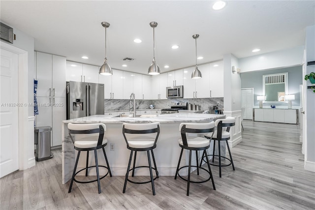 13850 NW 23rd St, Pembroke Pines, FL 33028 - kitchen with appliances with stainless steel finishes, light wood-style floors, backsplash, white cabinets, and a kitchen bar