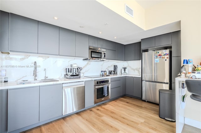 244 Biscayne Blvd Unit 4803, Miami, FL 33132 - kitchen with stainless steel appliances, gray cabinetry, decorative backsplash, modern cabinets, and light wood-type flooring