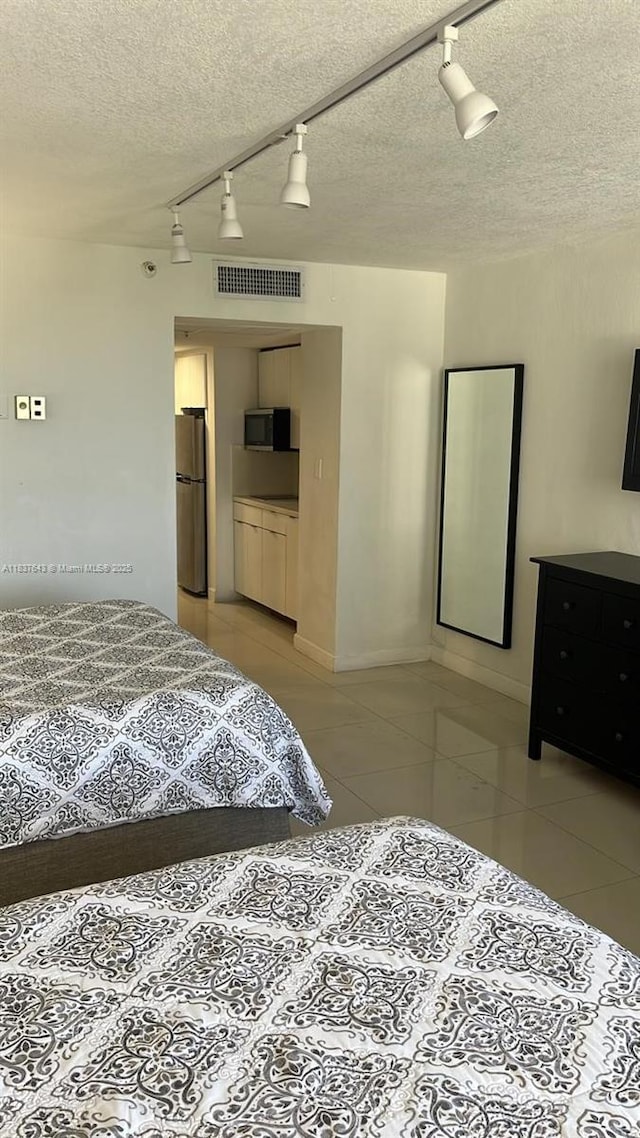 19201 Collins Ave Unit 330, Sunny Isles Beach, FL 33160 - bedroom featuring rail lighting, freestanding refrigerator, light tile patterned floors, and a textured ceiling