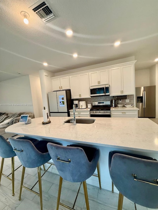 4468 Spruce Ln, Oakland Park, FL 33309 - kitchen featuring appliances with stainless steel finishes, a breakfast bar, white cabinets, decorative backsplash, and light stone countertops