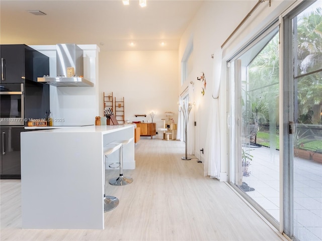 6110 Pitch Ln, Boynton Beach, FL 33437 - kitchen featuring wall chimney exhaust hood, healthy amount of natural light, a kitchen breakfast bar, and light wood-type flooring