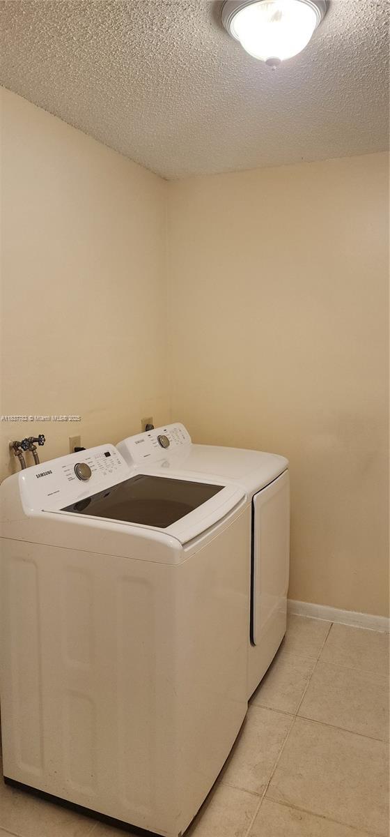 2957 Oak Park Cir, Davie, FL 33328 - laundry area with washer and clothes dryer, light tile patterned floors, and a textured ceiling