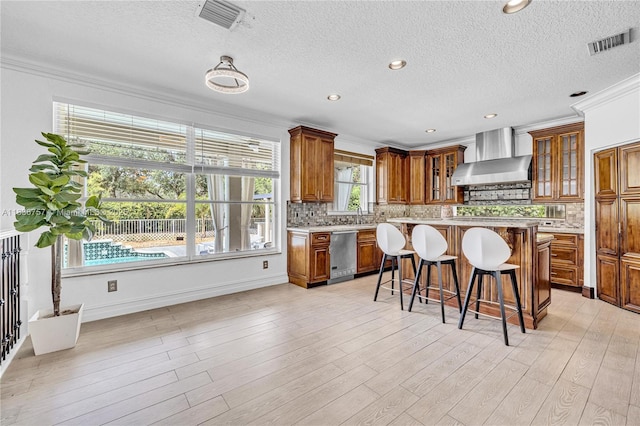 19480 SW 39th Ct, Miramar, FL 33029 - kitchen with wall chimney range hood, dishwasher, brown cabinetry, a breakfast bar area, and light countertops